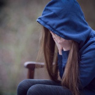 A stressed girl sitting on a bench while holding her face.