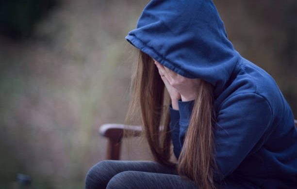 A stressed girl sitting on a bench while holding her face.
