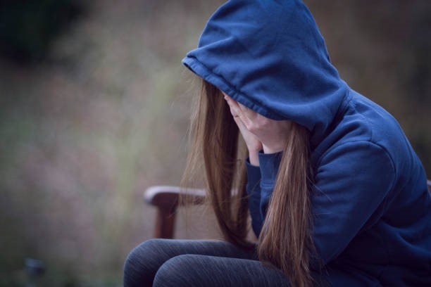 A stressed girl sitting on a bench while holding her face.