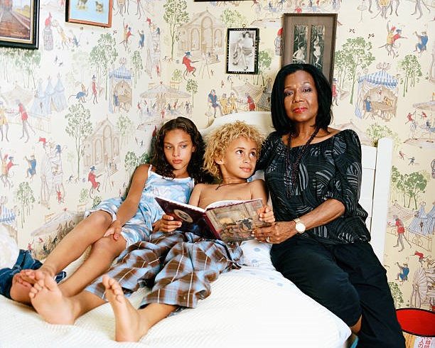 An older woman sitting on a bed with two children, reading a book together.