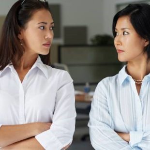 Two women standing face-to-face with crossed arms, looking at each other.