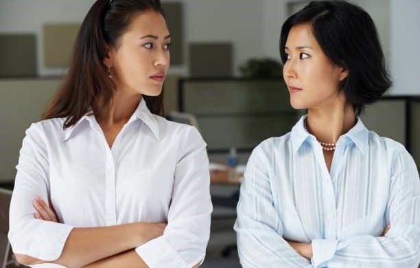 Two women standing face-to-face with crossed arms, looking at each other.