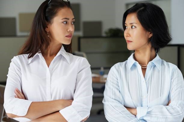 Two women standing face-to-face with crossed arms, looking at each other.