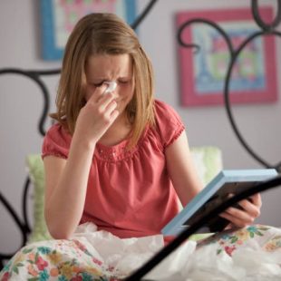 A young girl is sitting on a bed, crying while holding a photo frame.