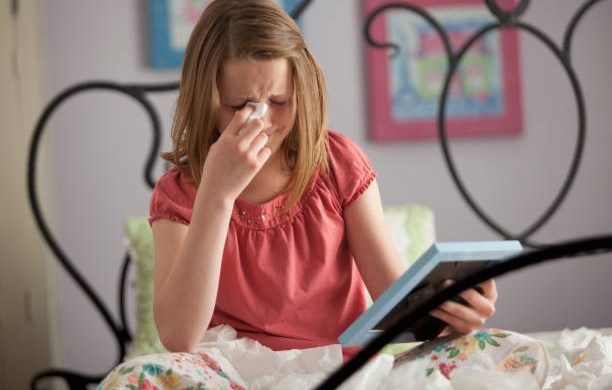 A young girl is sitting on a bed, crying while holding a photo frame.