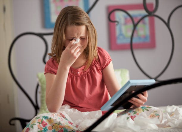 A young girl is sitting on a bed, crying while holding a photo frame.